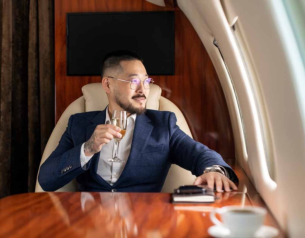 successful Asian businessman in suit and glasses sits in private jet and drinks champagne, Korean manager in business clothes flies in business class and looks out the window, luxury lifestyle